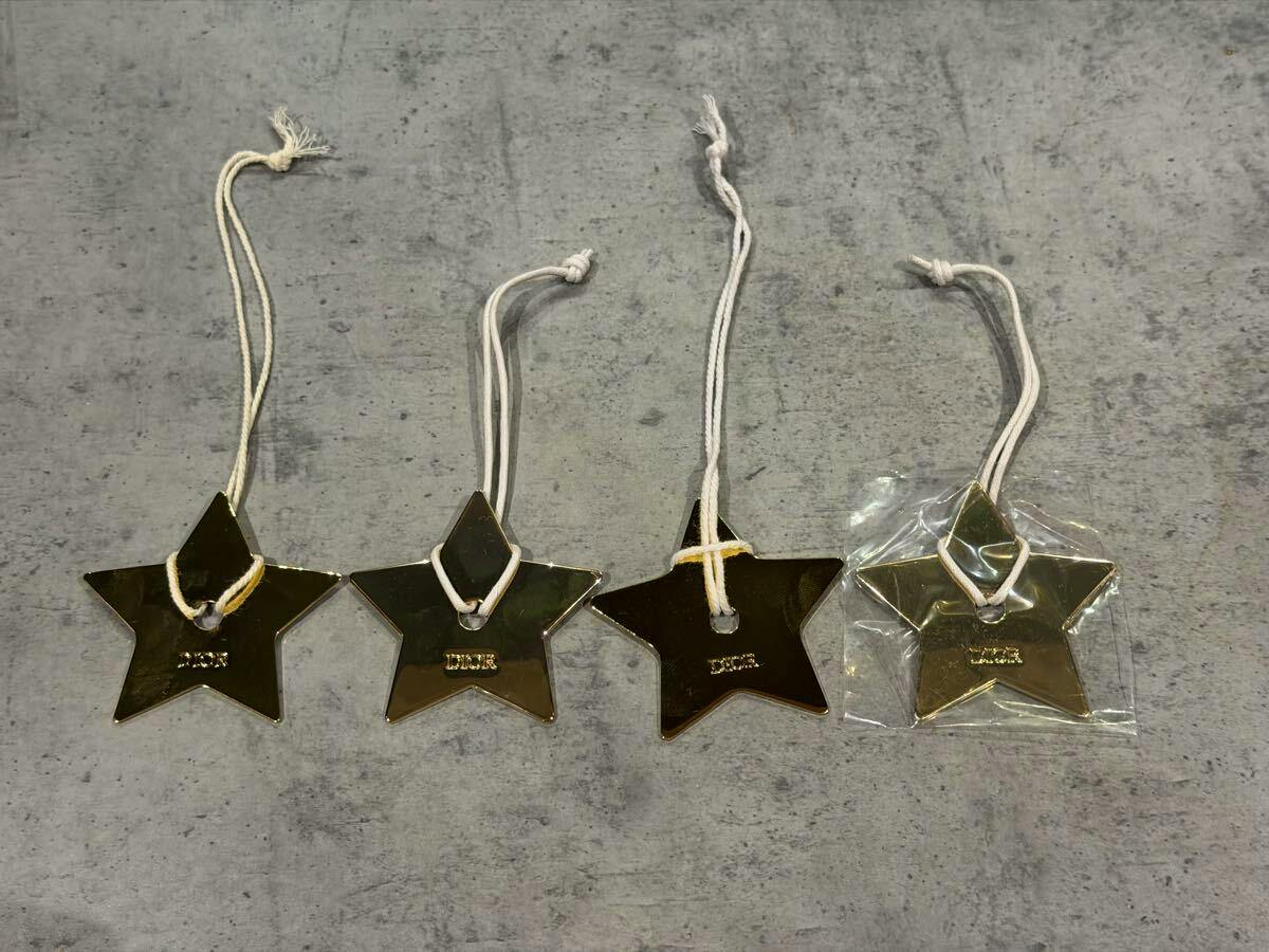 Four gold-tone star-shaped Dior keychain charms with white cords arranged on a gray surface.