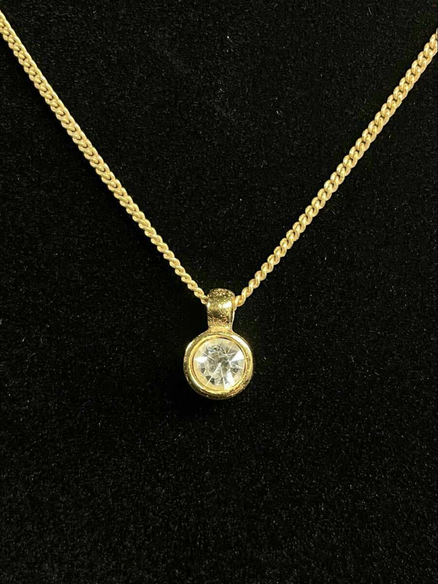 Close-up of a gold-tone necklace pendant with a clear round stone on a black background.