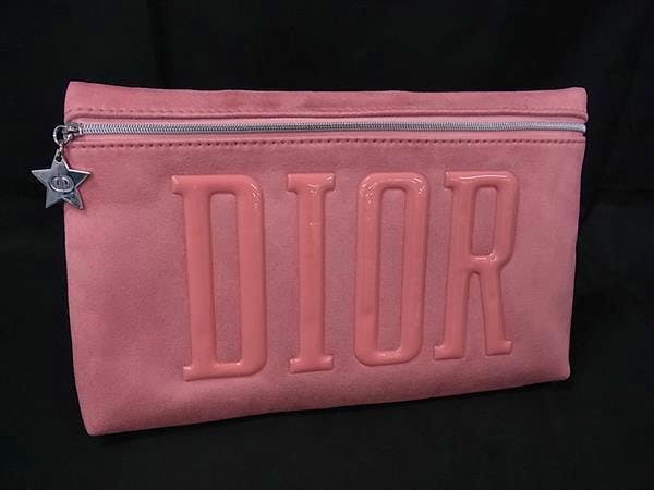 Pink suede Christian Dior clutch bag with raised DIOR lettering and a star zipper pull against a black background.
