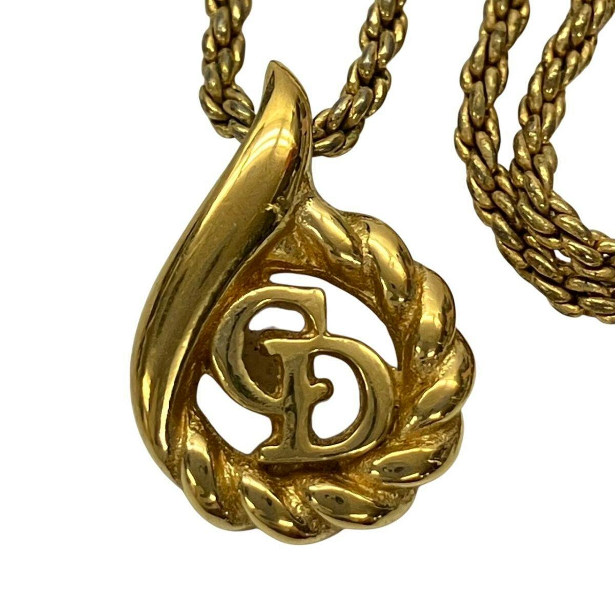 Close-up of a gold-colored teardrop necklace pendant with an interlocking "CD" logo and braided chain.