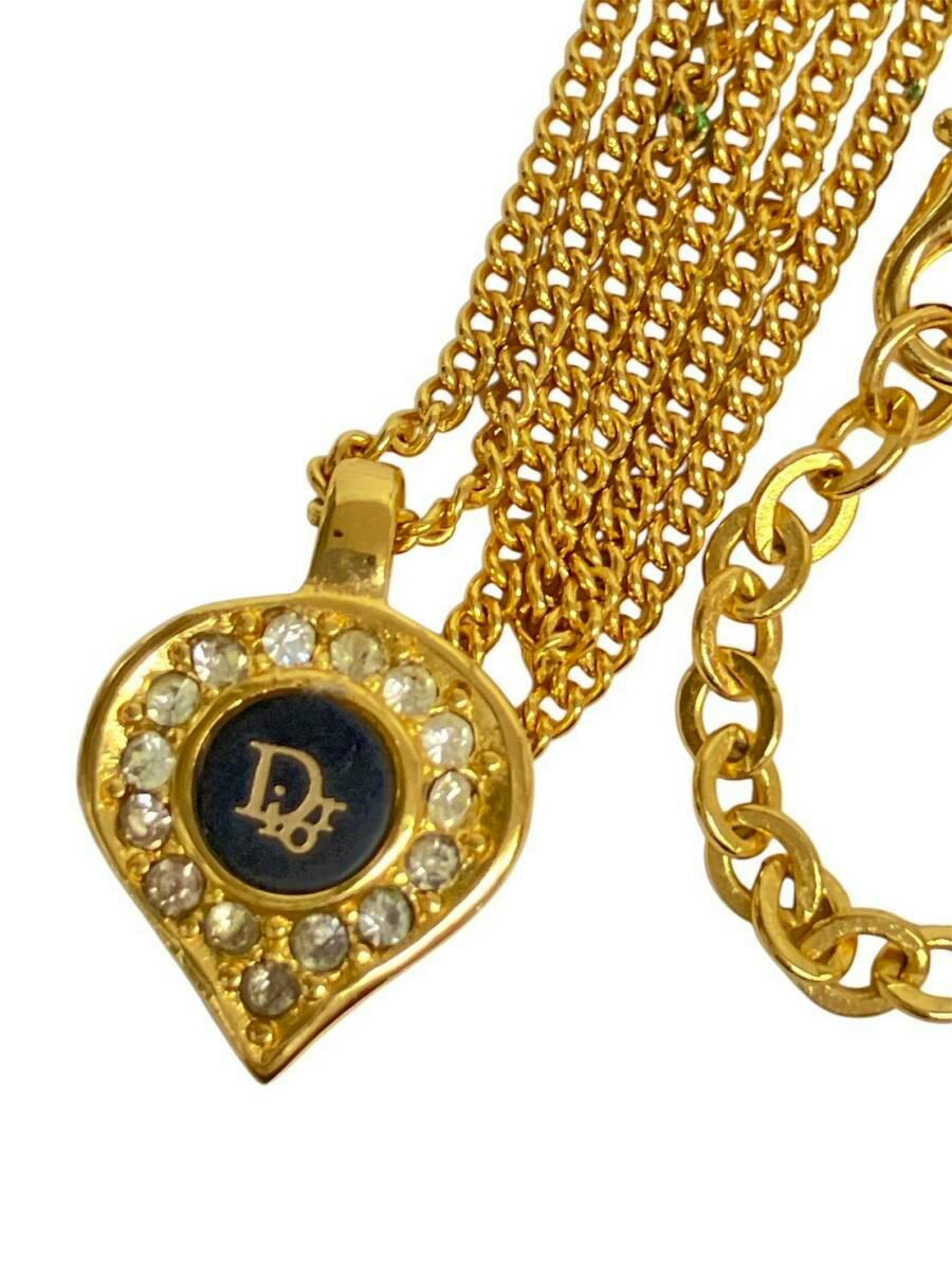 Close-up of a gold-color drop-shaped Christian Dior pendant with surrounding rhinestones and attached gold chains.