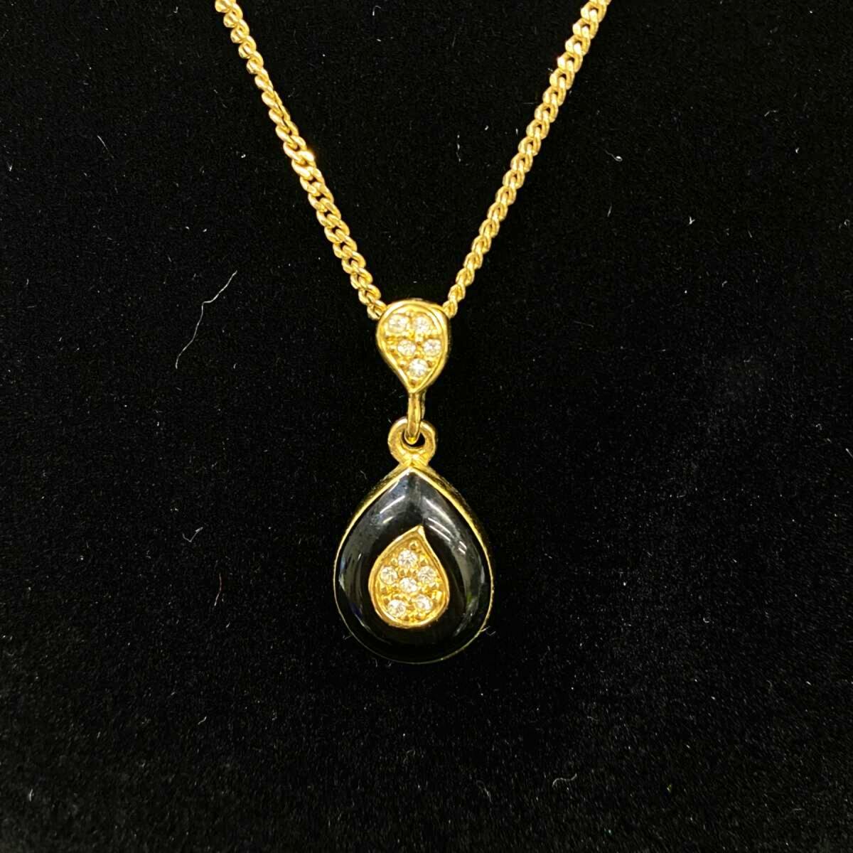 Gold-tone teardrop pendant necklace with black inlay and rhinestone accents shown on a black background.