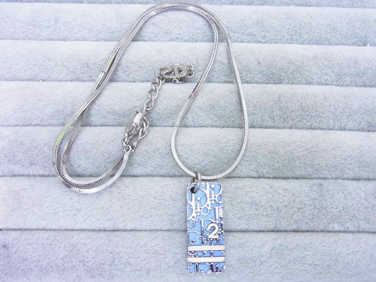 Silver-tone necklace laid on gray display with a rectangular light-blue patterned pendant showing a small '2' and a silver snake chain.