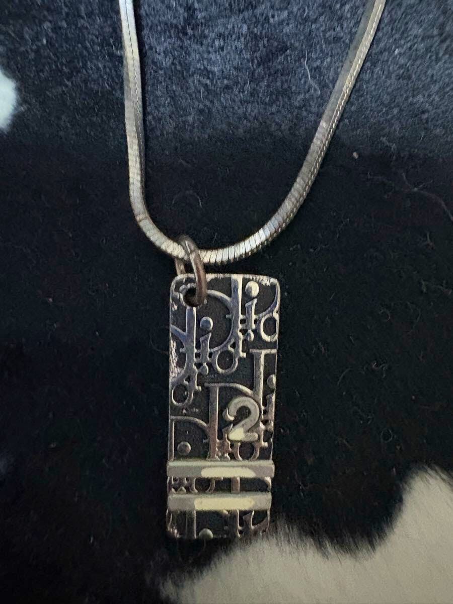 Christian Dior rectangular trotter-pattern black plate pendant hanging from a chain on a dark background.