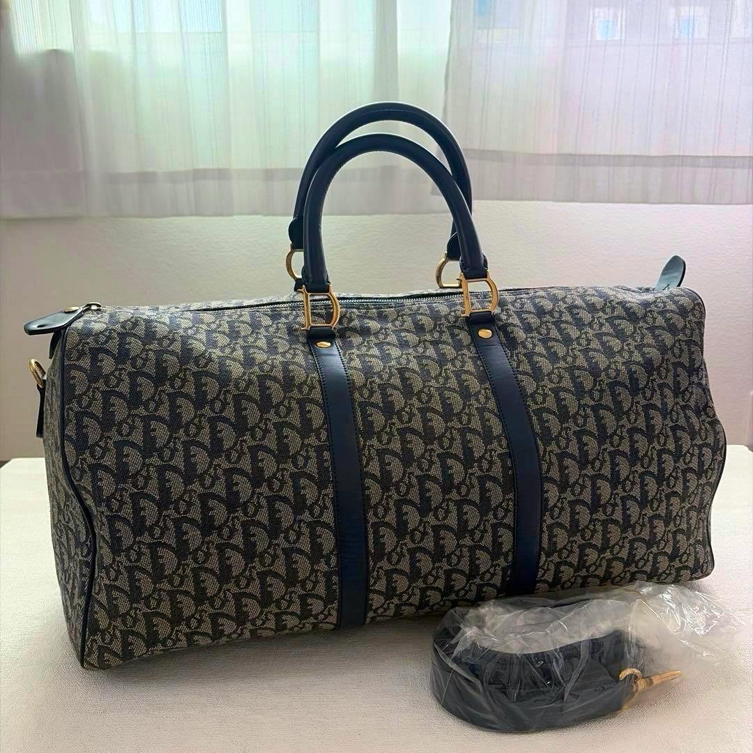 Christian Dior trotter canvas duffle bag with leather top handles and a wrapped shoulder strap placed in front.