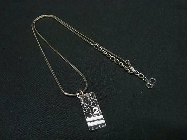 Silver-tone necklace with a rectangular patterned pendant and chain laid on a black background.