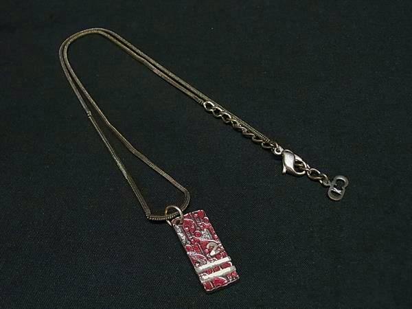 Christian Dior necklace with a rectangular pink patterned pendant on a silver-tone chain laid on a black background.