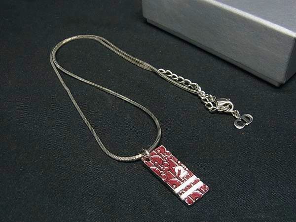Silver-tone Christian Dior necklace with a rectangular red patterned pendant and chain displayed on a black background next to a gray box.