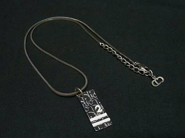 Christian Dior silver and black Trotter pendant necklace laid flat on a dark background showing the pendant and chain.