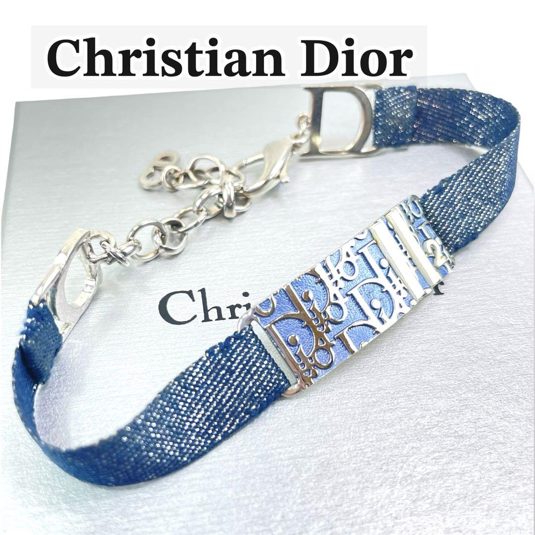 Close-up of a Christian Dior fabric bracelet with a blue woven band and a silver-tone decorative plate bearing a Dior motif.
