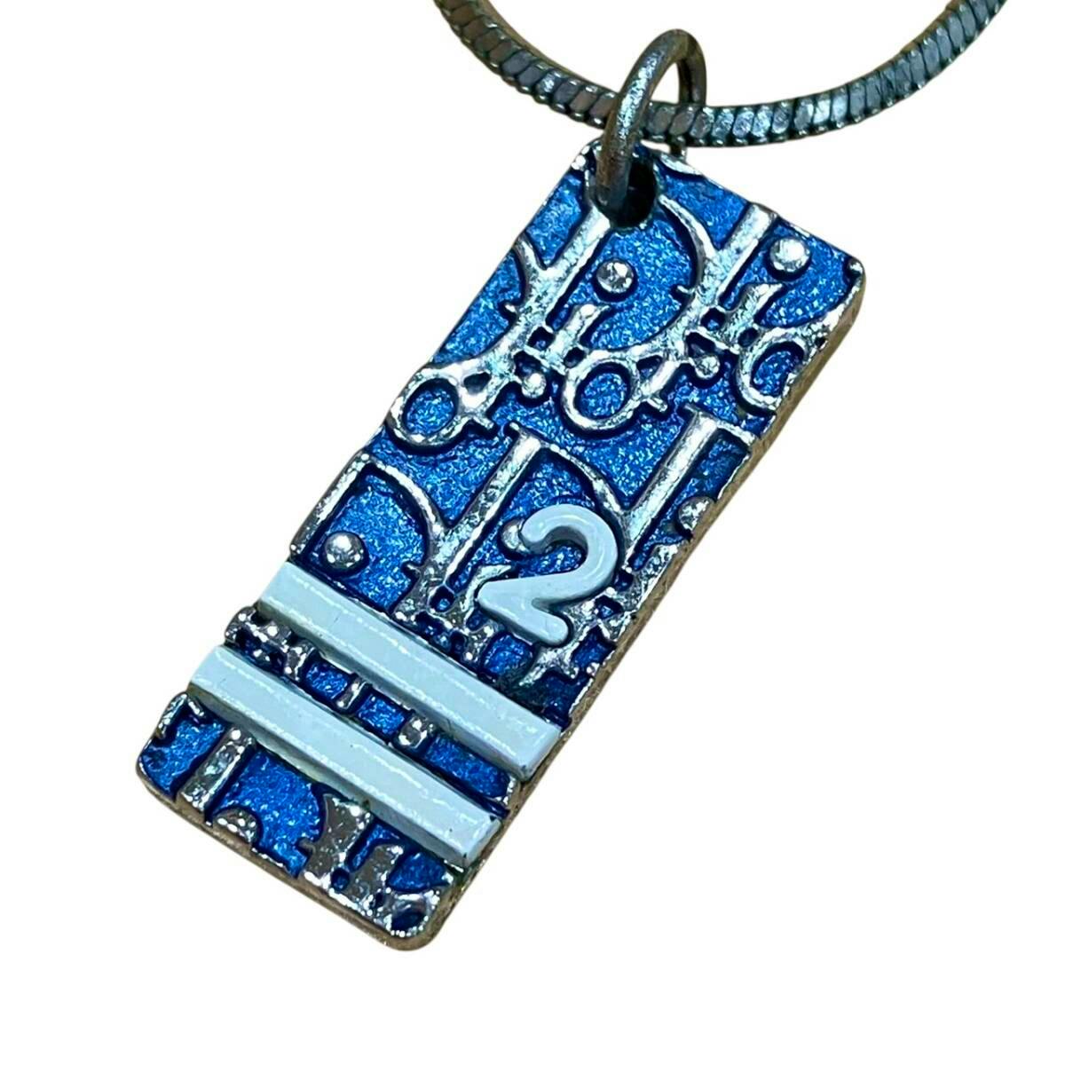 Close-up of a blue rectangular Dior trotter-plate pendant hanging from a necklace chain.
