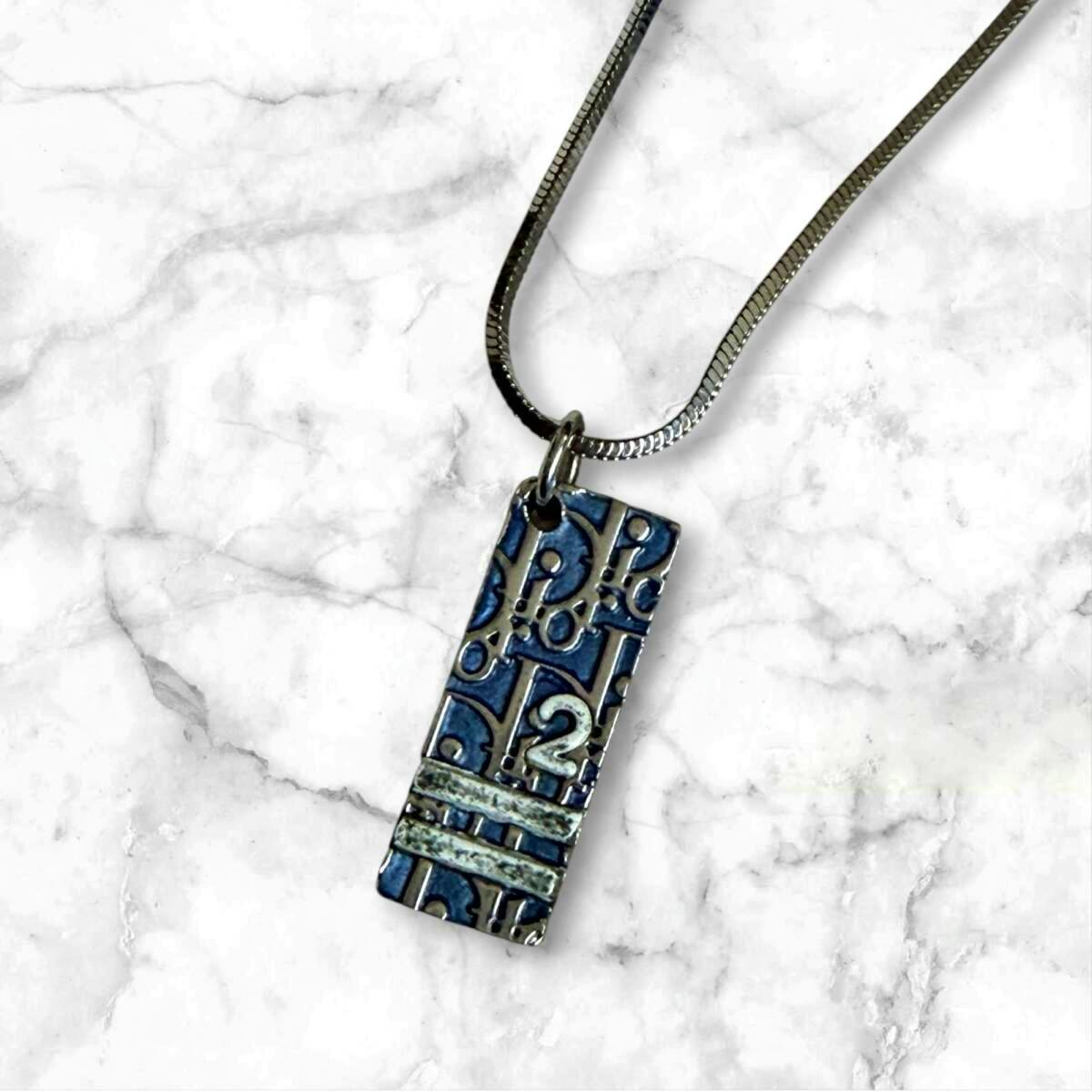 Close-up of a Christian Dior rectangular trotter-pattern plate pendant on a silver-tone necklace.