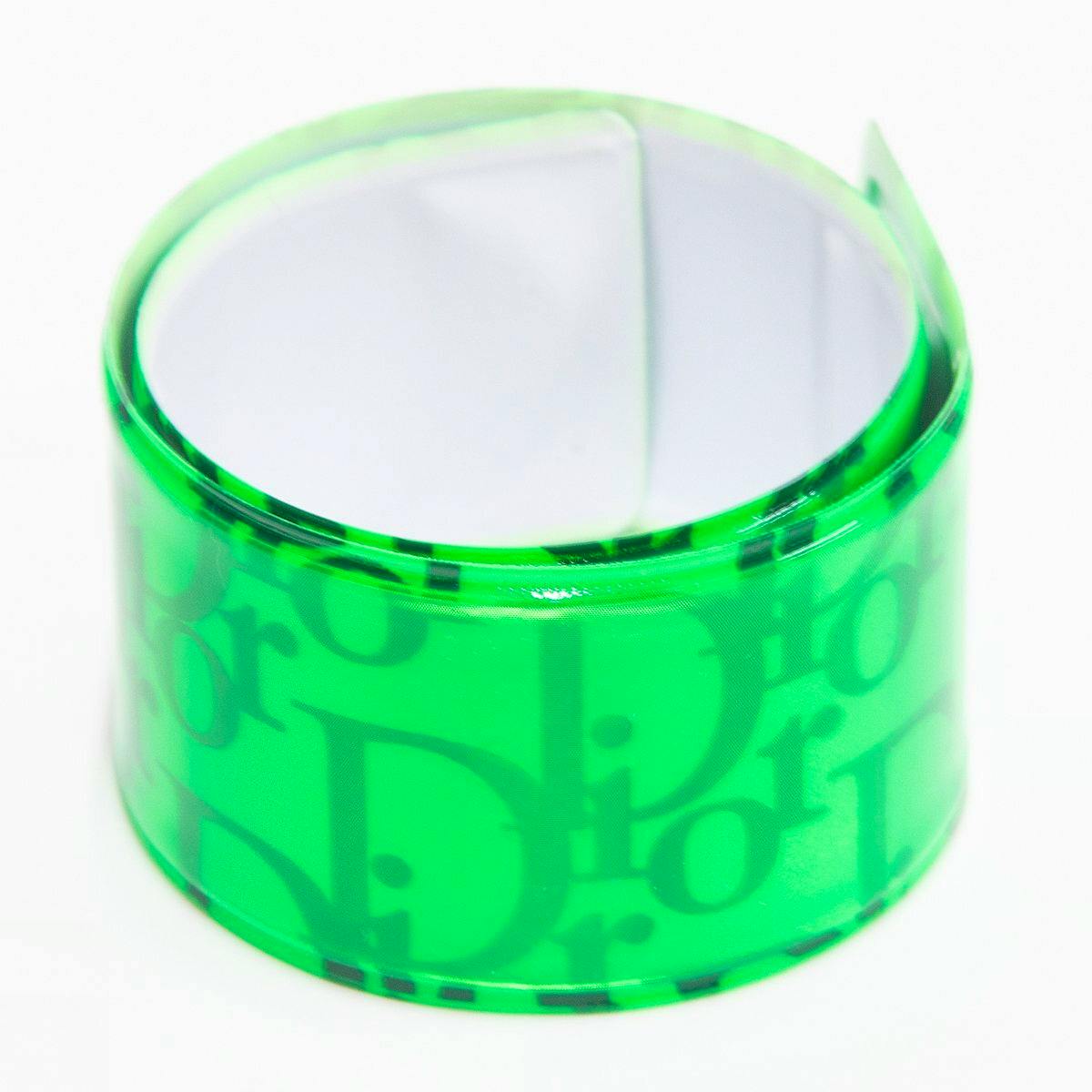 Green Christian Dior reflective slap-style plastic wristband rolled into a loop showing the Dior logo pattern.