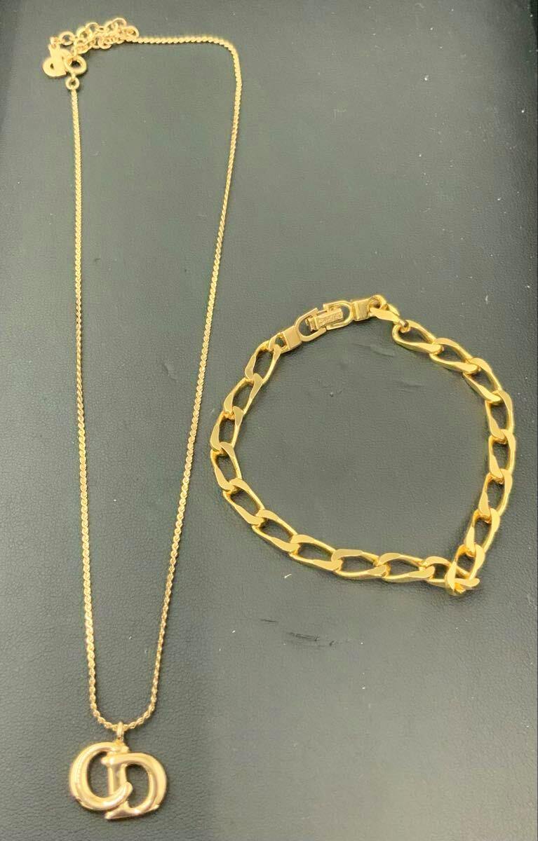 A gold-tone Christian Dior necklace with interlocking CD logo pendant and a gold chain bracelet displayed on a dark surface.