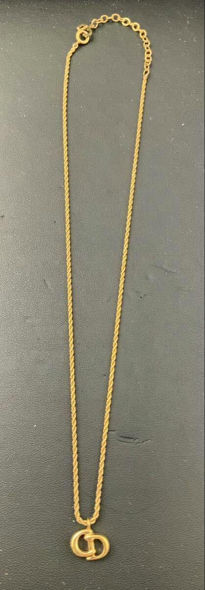 Gold-colored Christian Dior necklace with interlocking CD logo pendant laid flat on a dark surface.