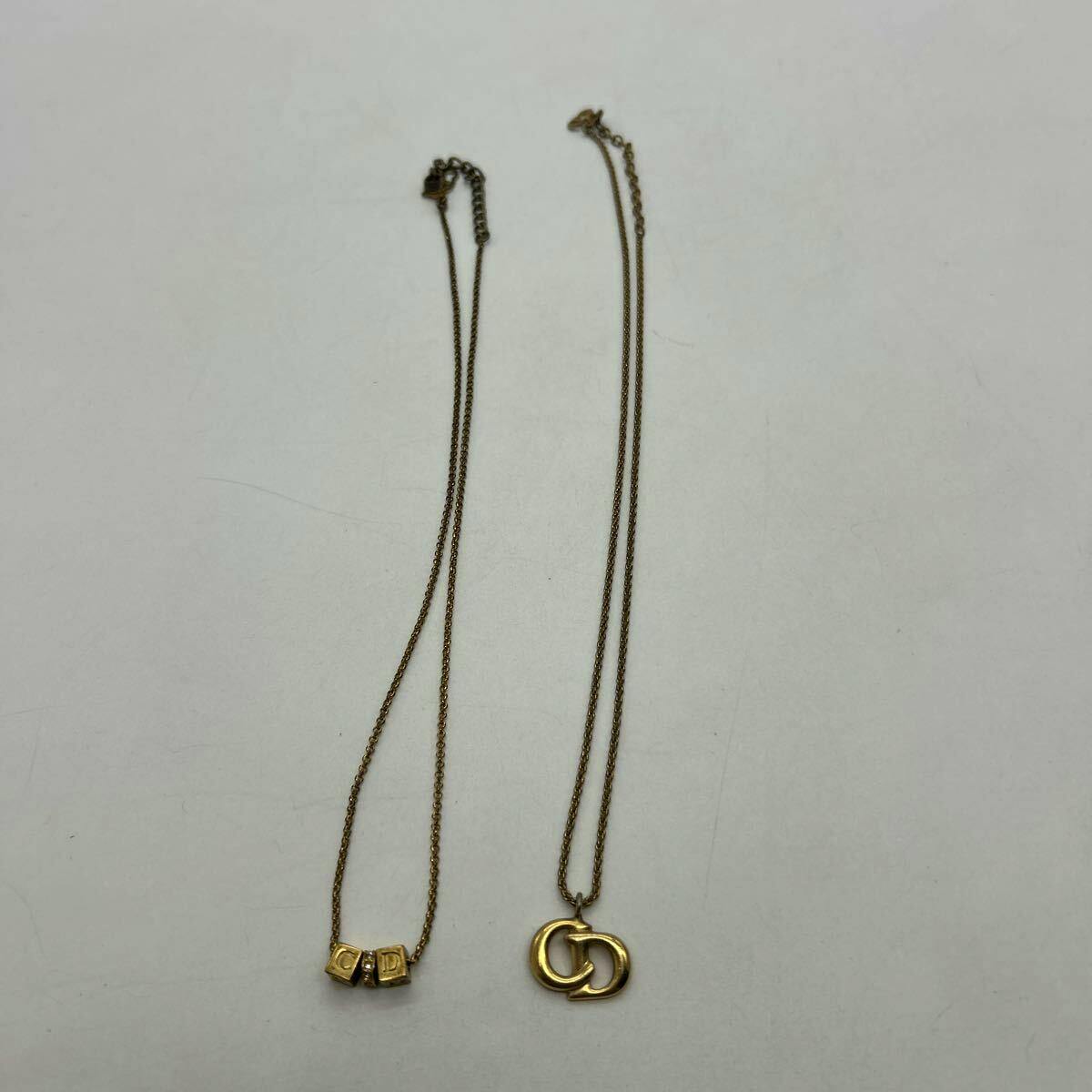 Two Christian Dior gold-color necklaces with CD logo pendants laid flat on a white background.