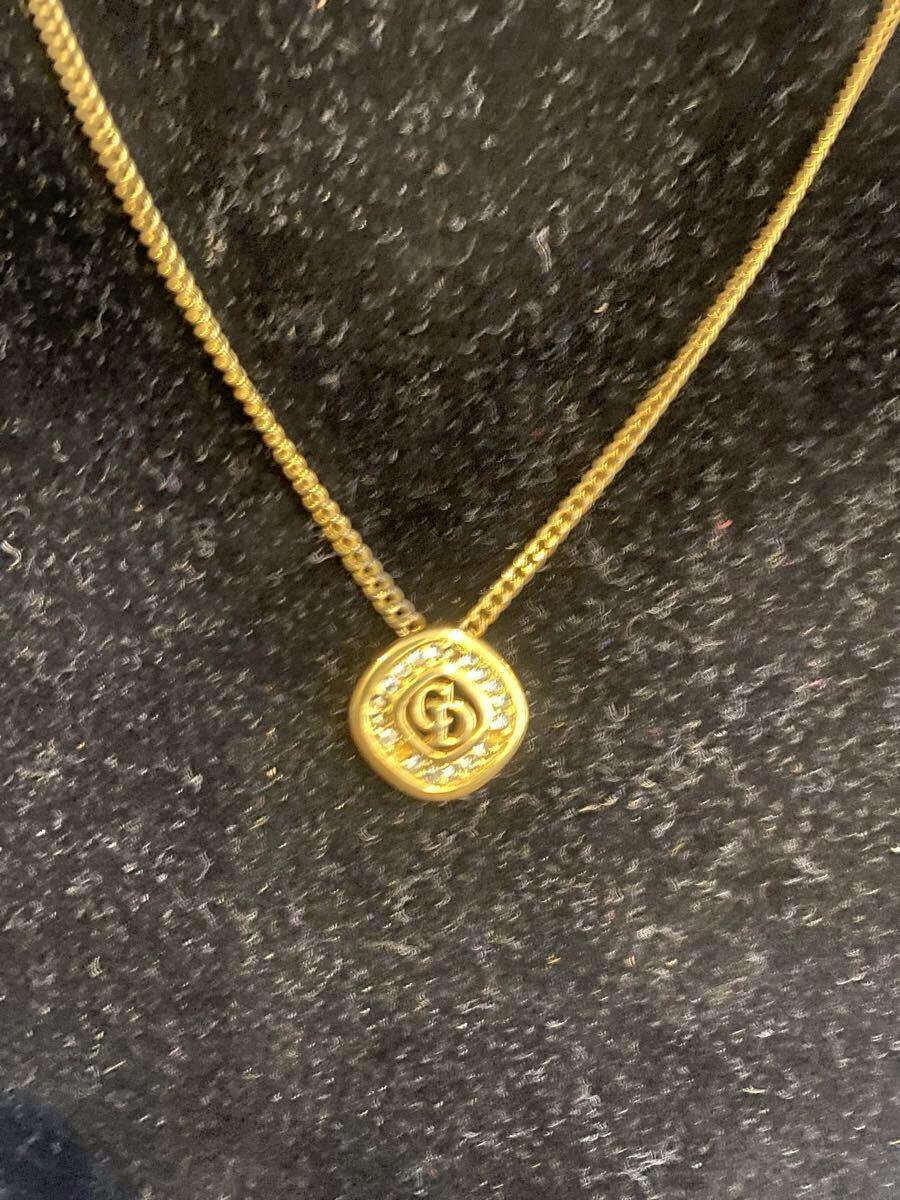 Gold-color Christian Dior necklace with a round CD logo pendant set with rhinestones on a black fabric background.