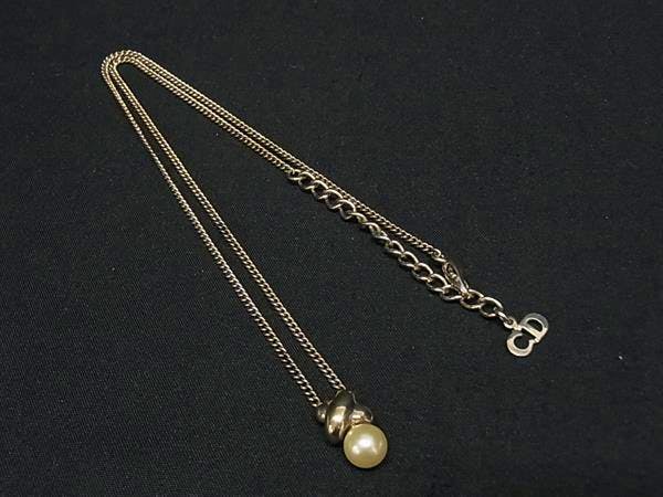 Gold-tone Christian Dior necklace with a single pearl pendant and CD logo charm laid on black fabric.