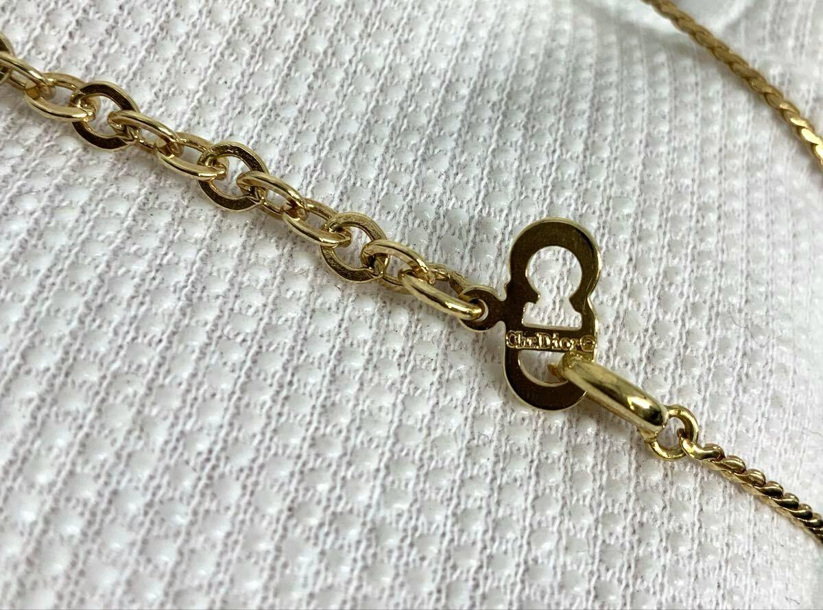 Close-up of a gold-tone Christian Dior necklace chain and clasp stamped "Ch.Dior" on a white textured fabric background.
