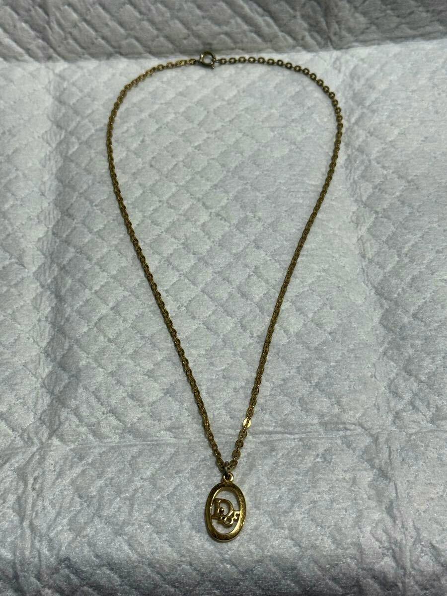 Gold-color Christian Dior necklace with an oval Dior-logo pendant laid flat on a textured white background.