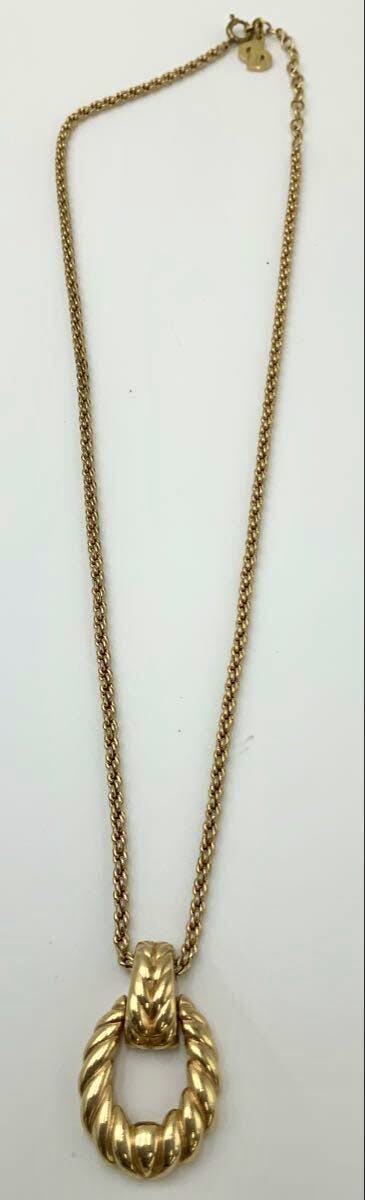 Gold-tone necklace with a twisted rope-style circular pendant on a chain photographed on a white background.