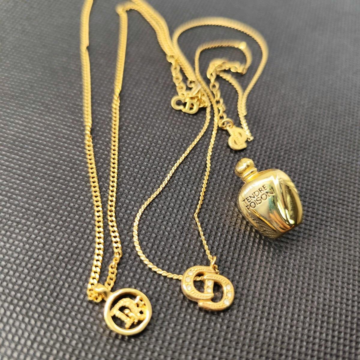 Several gold-tone Christian Dior necklaces and pendants, including CD logo charms and a small perfume-bottle charm, displayed on a black textured surface.