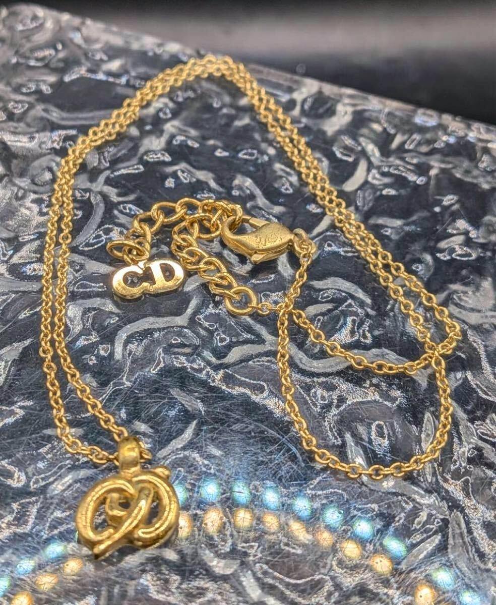 Gold-colored Christian Dior necklace with CD logo pendant and lobster clasp displayed on a textured background.