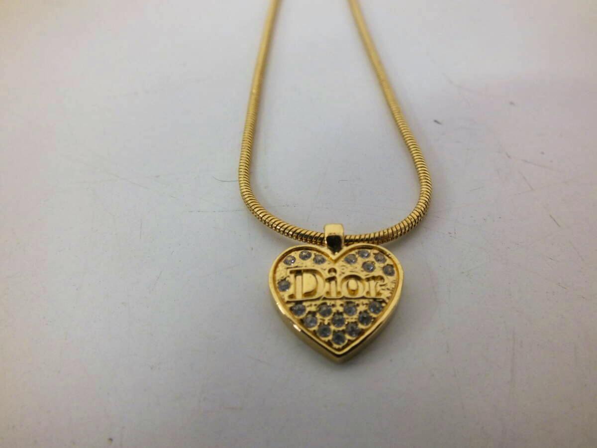 Gold-colored heart pendant necklace with a prominent "Dior" logo and small clear stones on a snake chain.