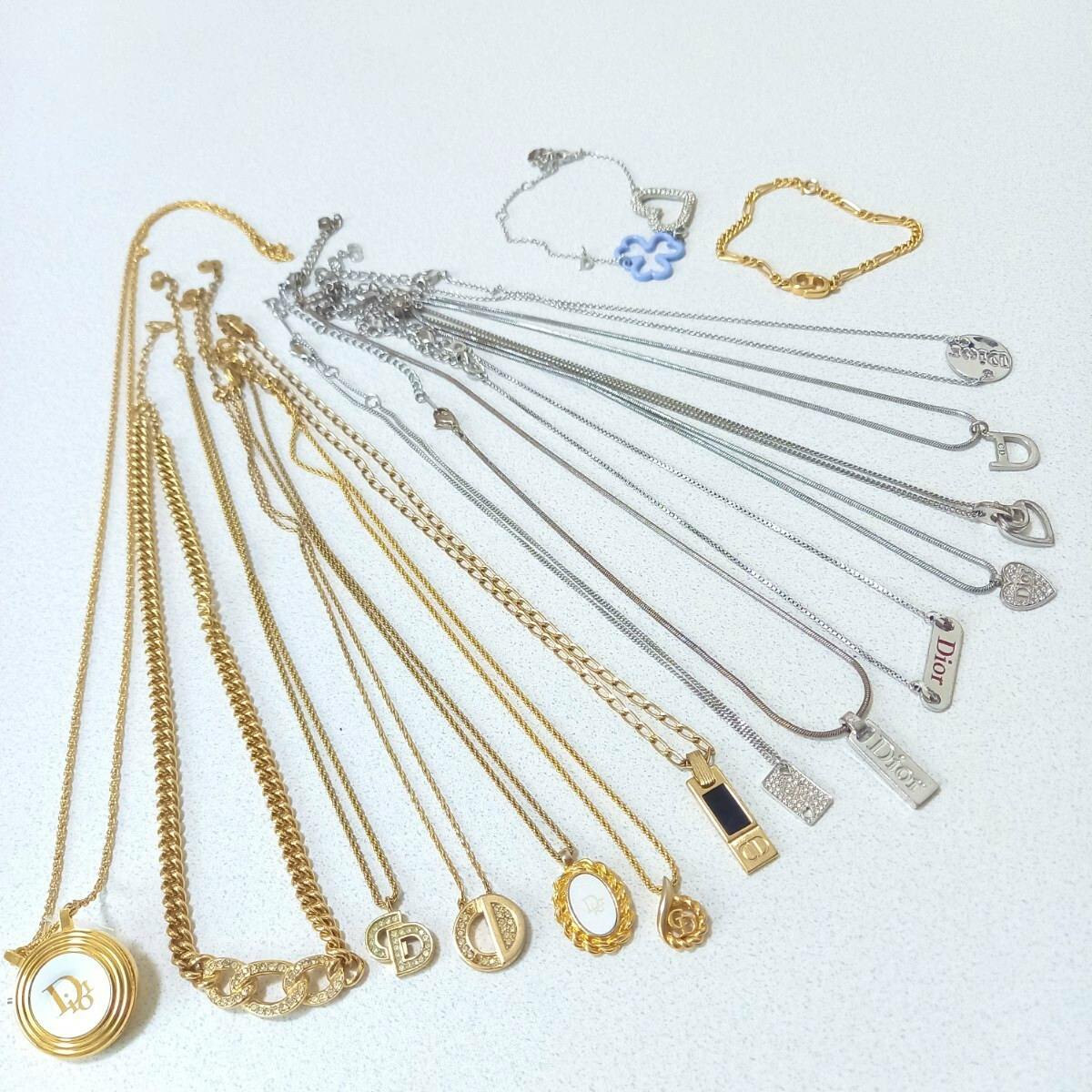 Several gold and silver Dior necklaces and bracelets arranged on a white surface, showing various chains and pendants.