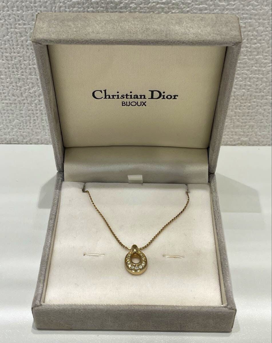 Gold-colored Christian Dior necklace with a circular pendant displayed in an open Christian Dior jewelry box.