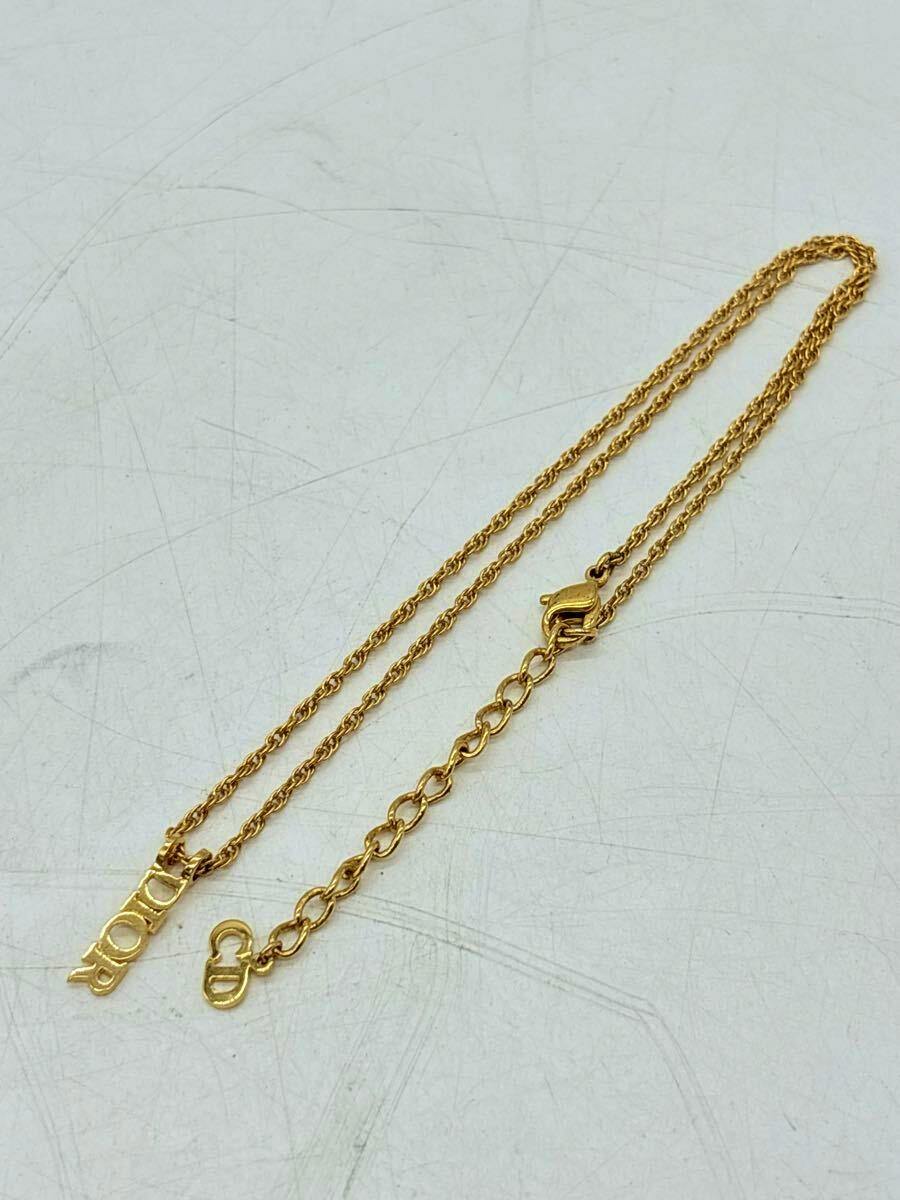 Gold-colored Christian Dior necklace laid flat on a white surface showing the chain, DIOR logo pendant, extender links, and lobster clasp.