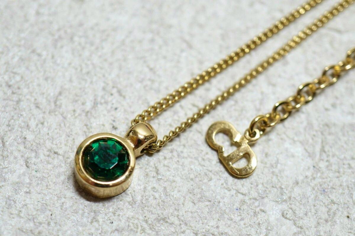 Gold-colored Christian Dior necklace with a small round pendant set with a green stone and a short chain showing a Dior logo charm.