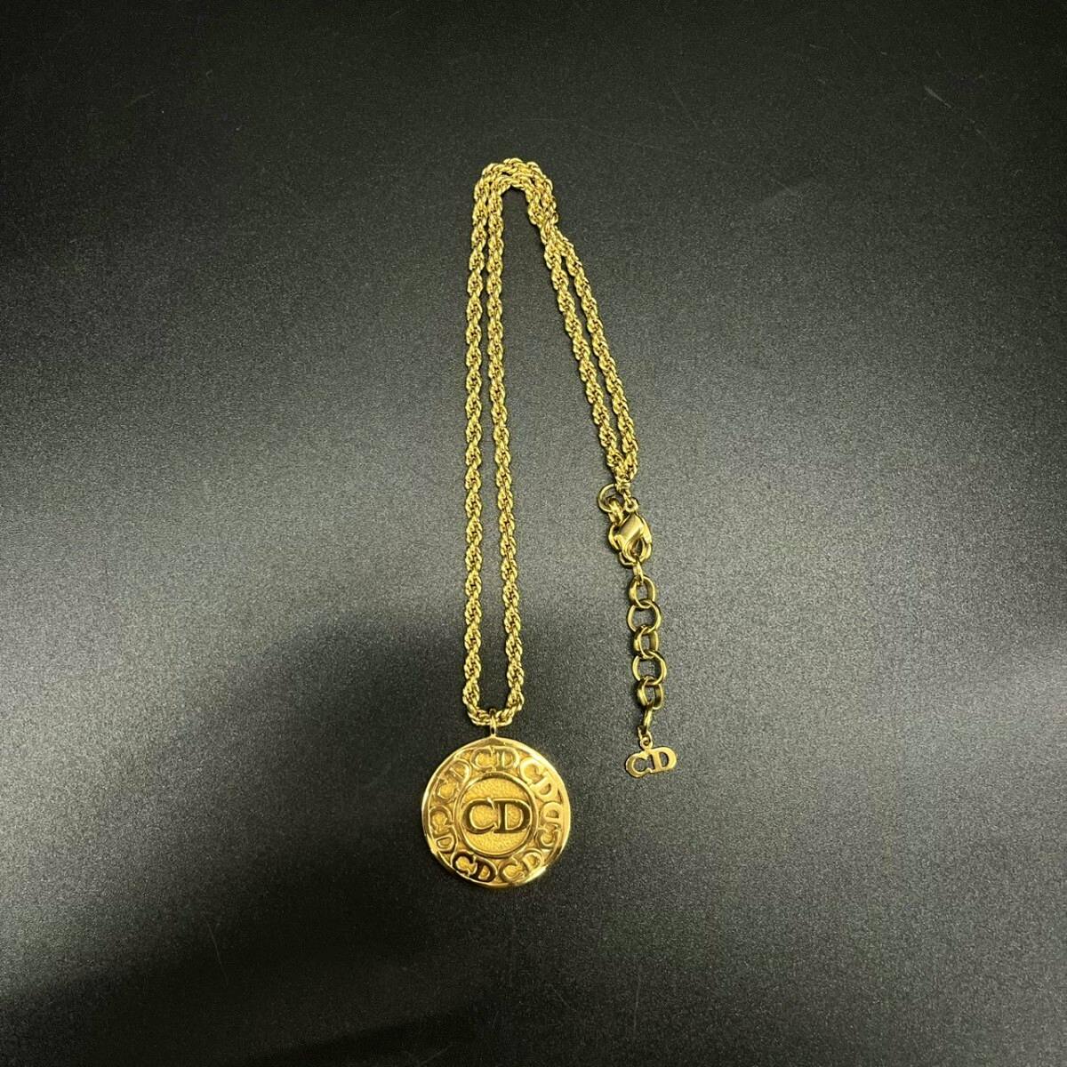 Gold-colored Christian Dior necklace with a round CD medallion and twisted chain on a black background.