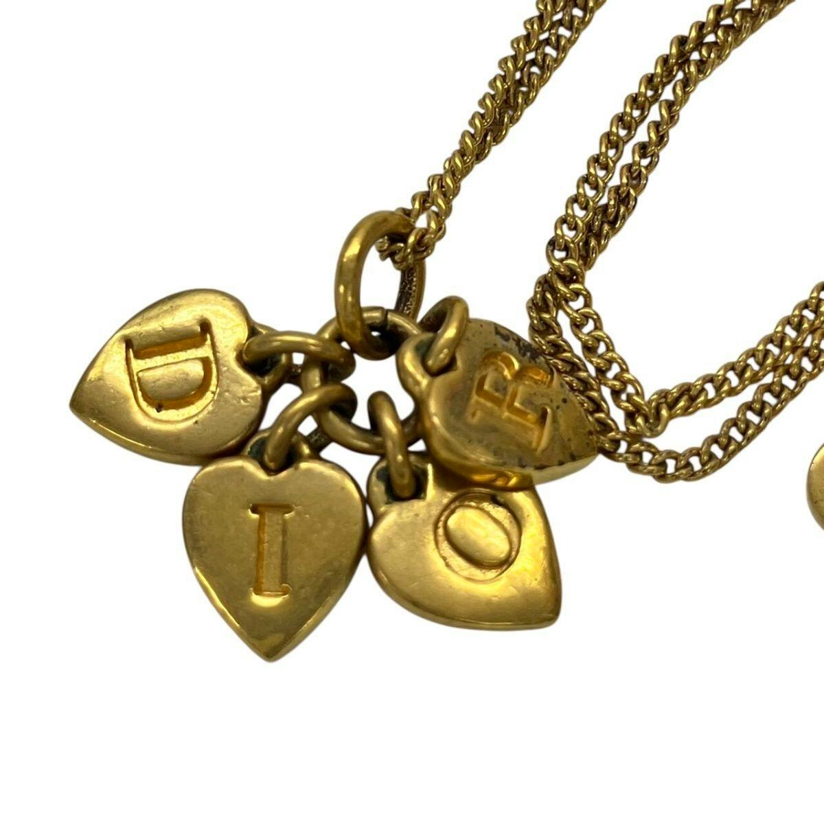 Close-up of a gold-colored necklace showing several heart-shaped logo charms on a chain.