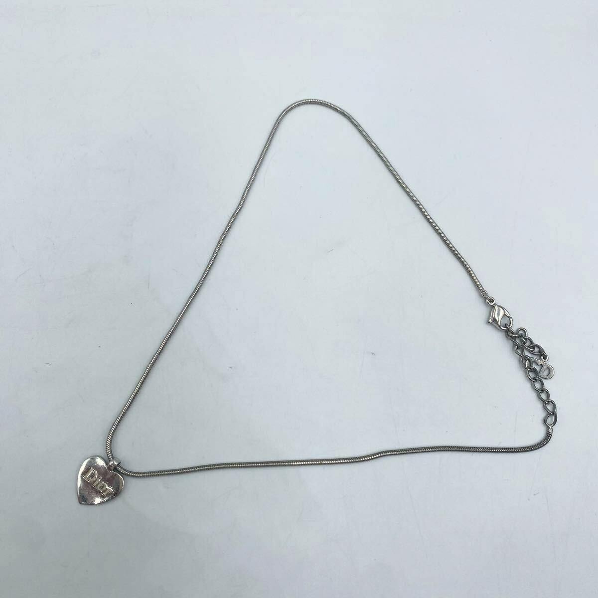 A heart-shaped Christian Dior logo pendant on a silver-tone necklace laid flat on a white background.