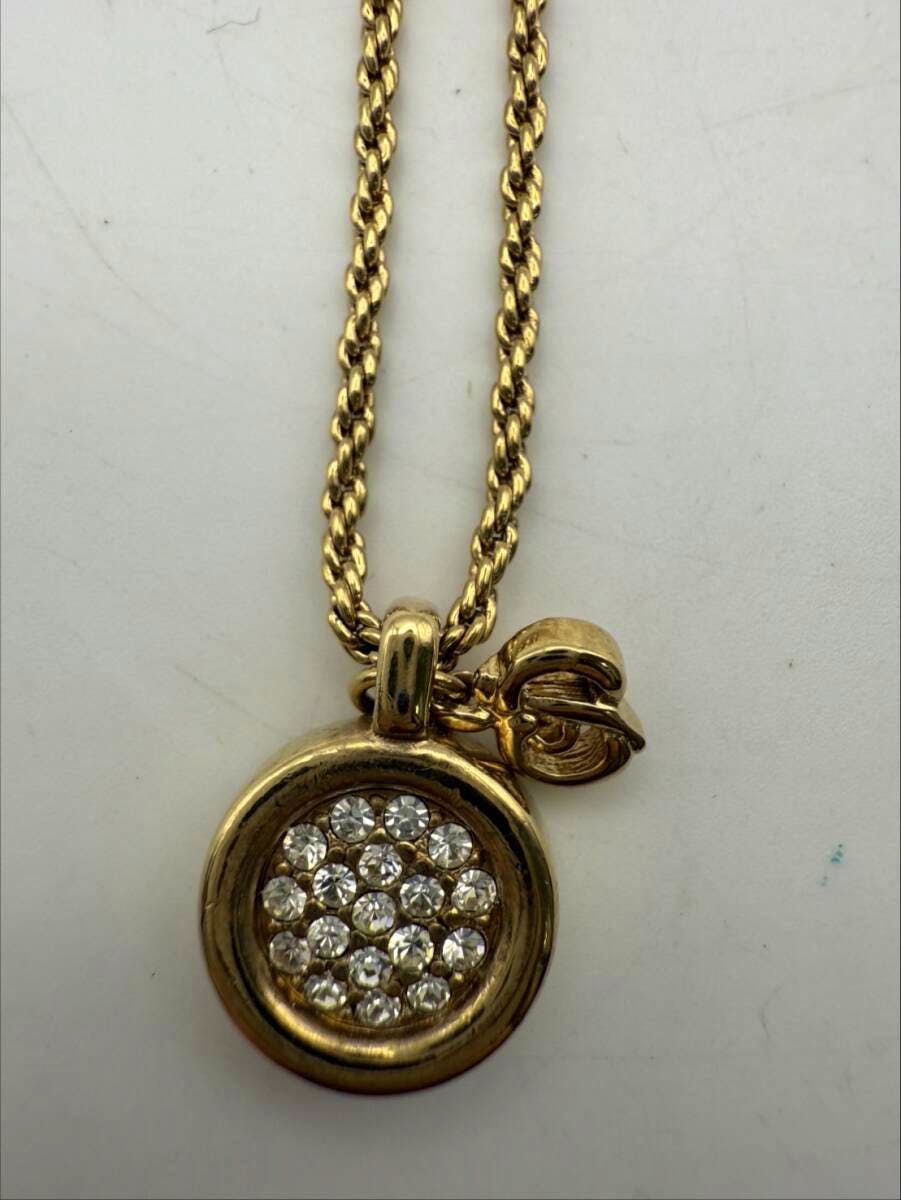 Close-up of the Christian Dior gold-tone necklace pendant showing a circular cluster of clear stones and a small charm on a gold chain.