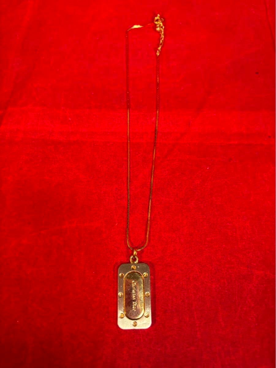 A gold-toned Christian Dior vintage plate-bis design necklace with rectangular pendant and chain laid on red fabric.