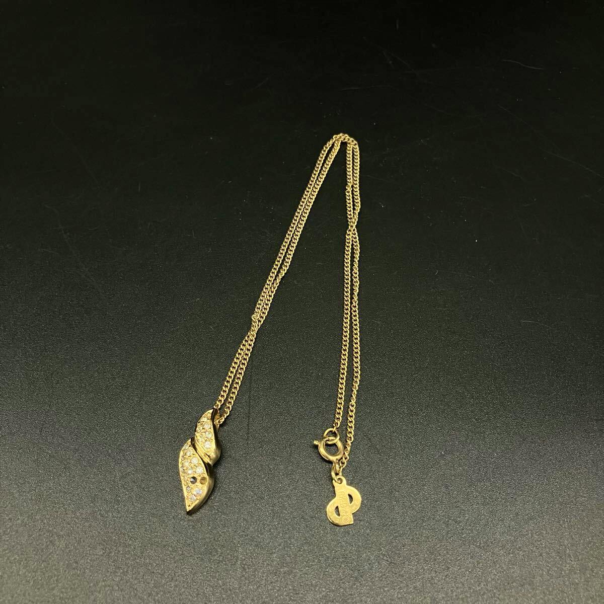Gold-colored Christian Dior necklace with a rhinestone-studded leaf-shaped pendant and chain laid flat on a black background.