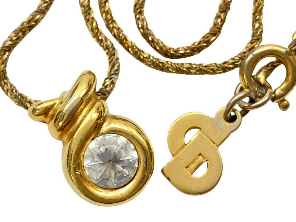 Close-up of a gold-colored Christian Dior necklace showing the twisted chain, a rhinestone-set pendant, and a CD logo charm near the clasp.