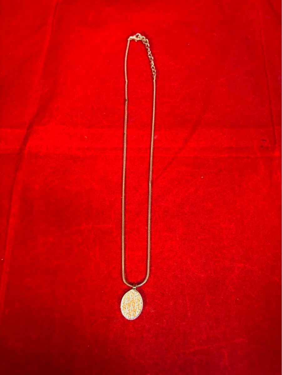 Christian Dior vintage trotter-pattern pendant necklace laid flat on red fabric, showing the full chain and oval pendant.