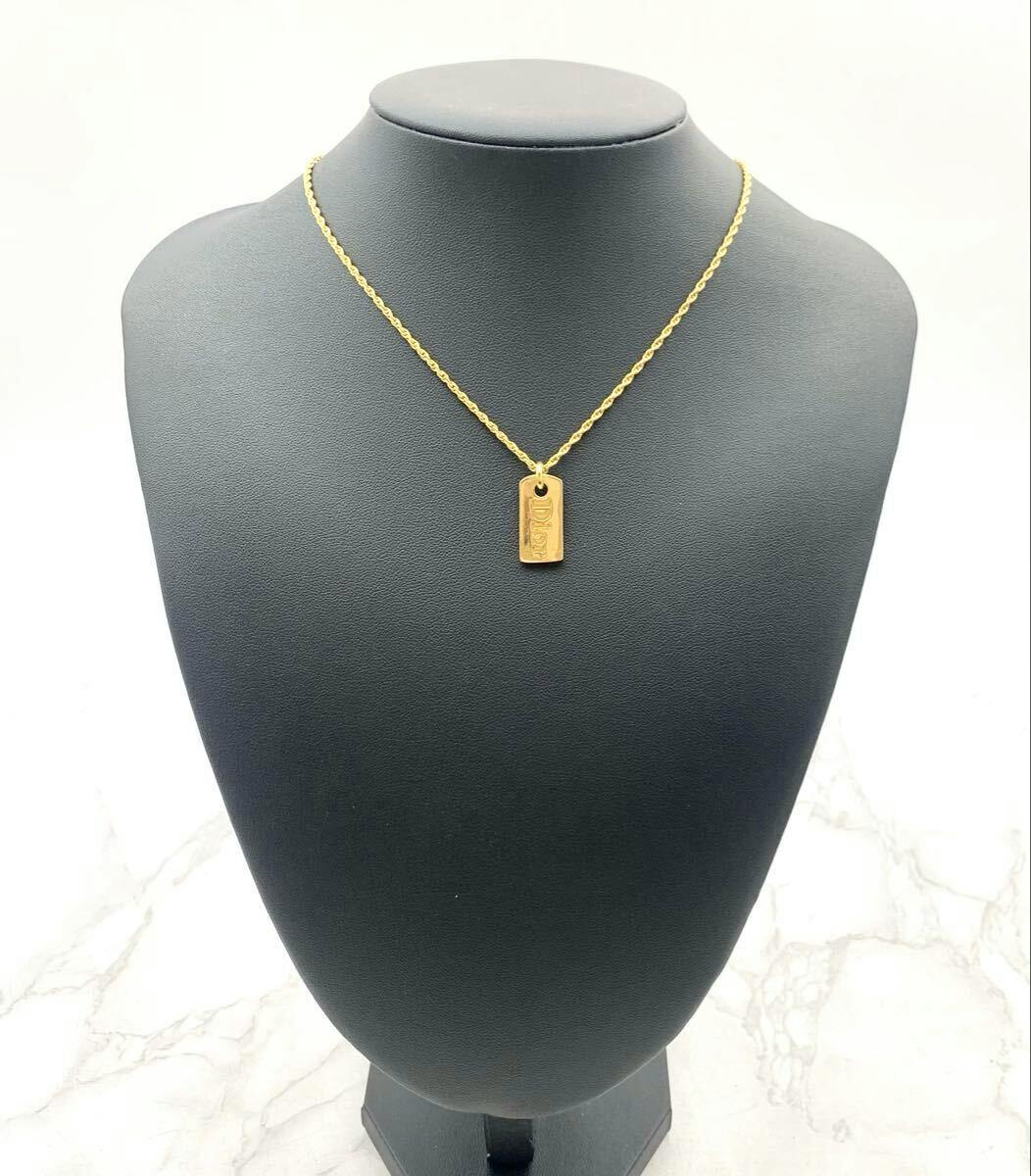 Gold-tone Christian Dior necklace with a rectangular tag engraved “Dior” displayed on a black bust.