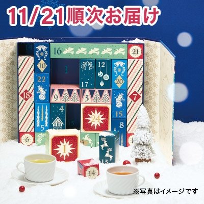 A Christmas-themed advent calendar box for black tea bags with numbered doors, shown with two cups of tea and a small decorative tree.
