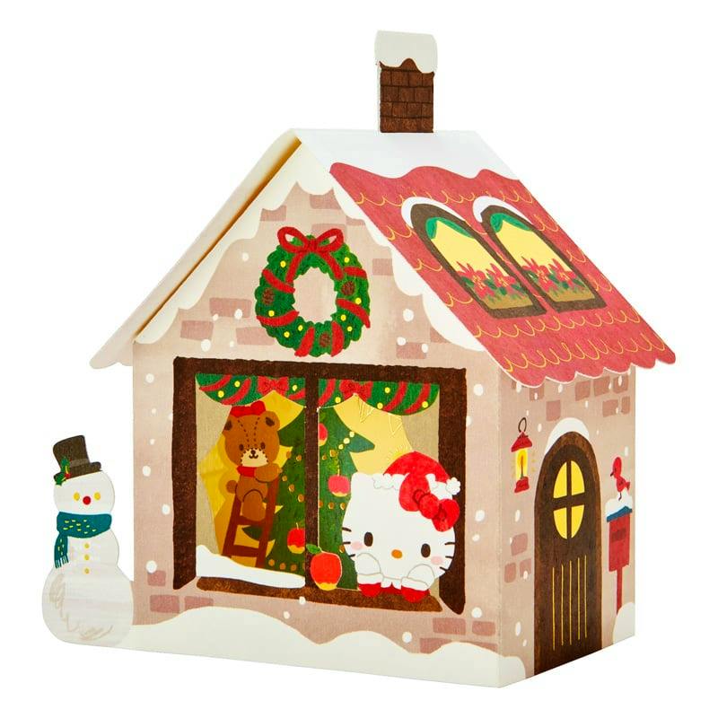 A house-shaped Christmas greeting card featuring Hello Kitty peeking from a window with a teddy bear inside and a snowman outside.