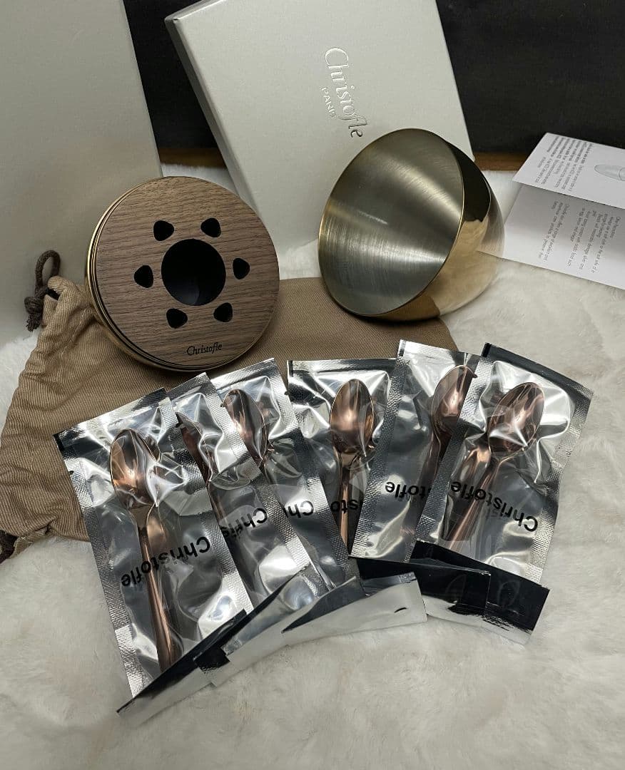 A stainless-steel bowl, six individually packaged spoons, a wooden lid with holes, a cloth pouch, and a box displayed on a soft surface.