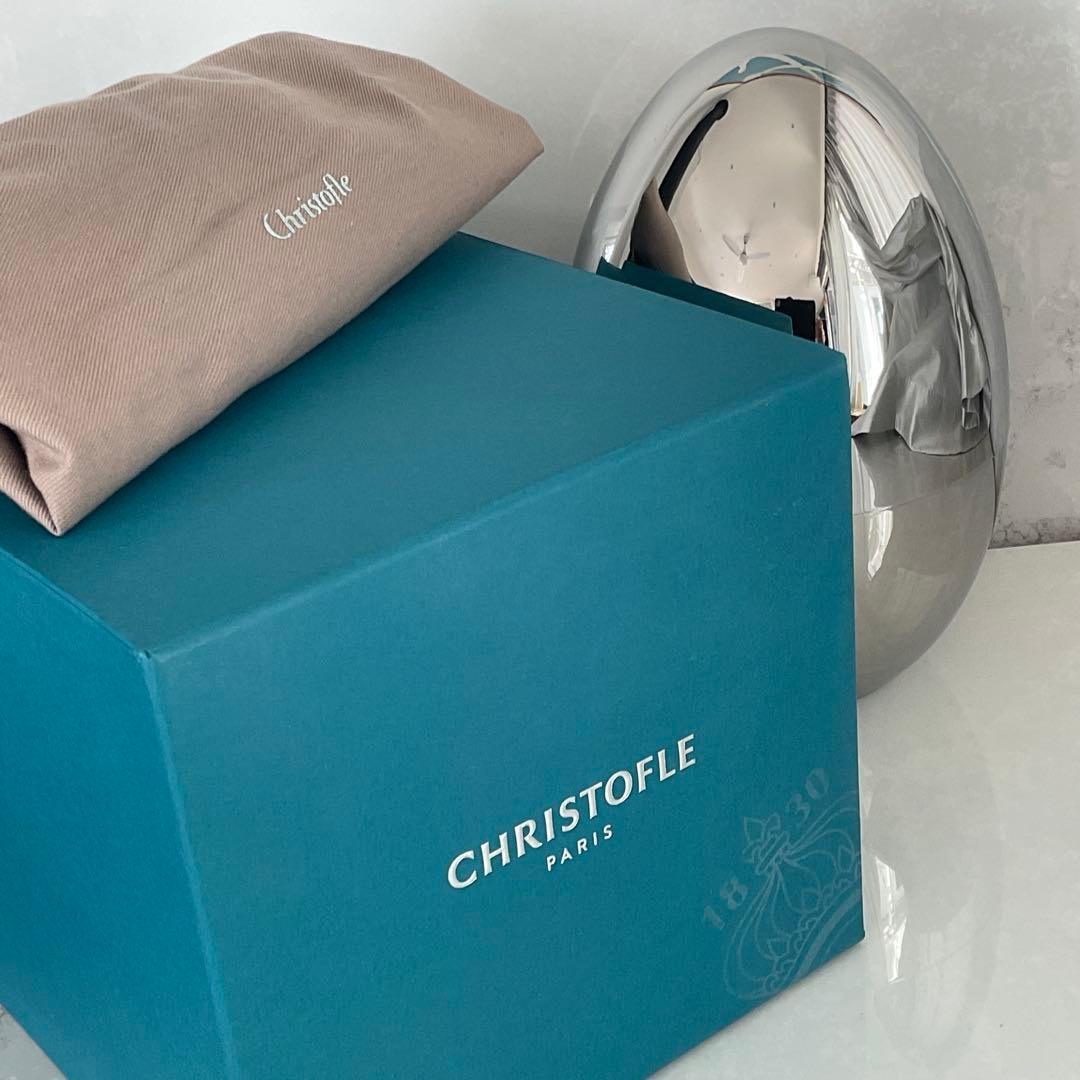 A blue Christofle case box with a beige Christofle cloth pouch and a reflective stainless steel Mood bowl beside it.