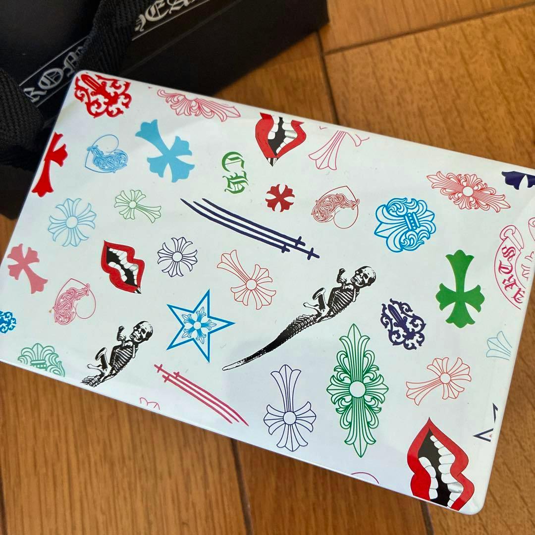 Top of a Chrome Hearts cookie tin showing multicolored motifs on a wooden floor.