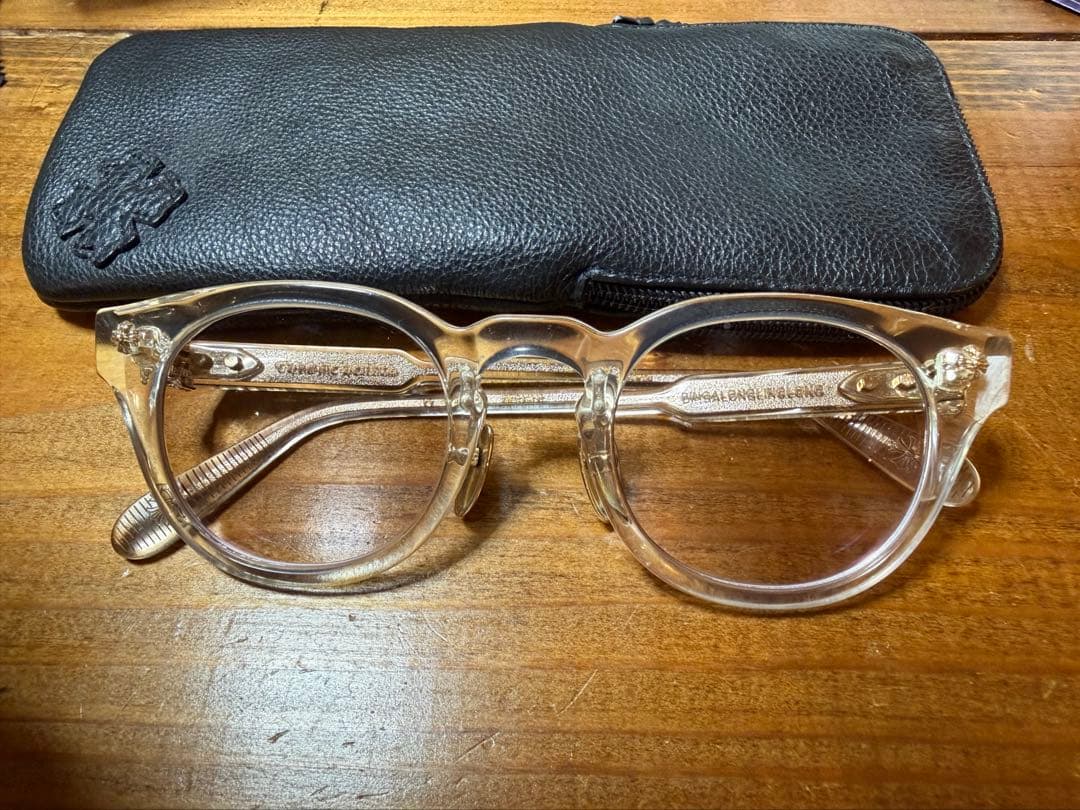 CHROME HEARTS DINGALONGLINGLONG glasses with clear frames shown in front of a black case on a wooden surface.