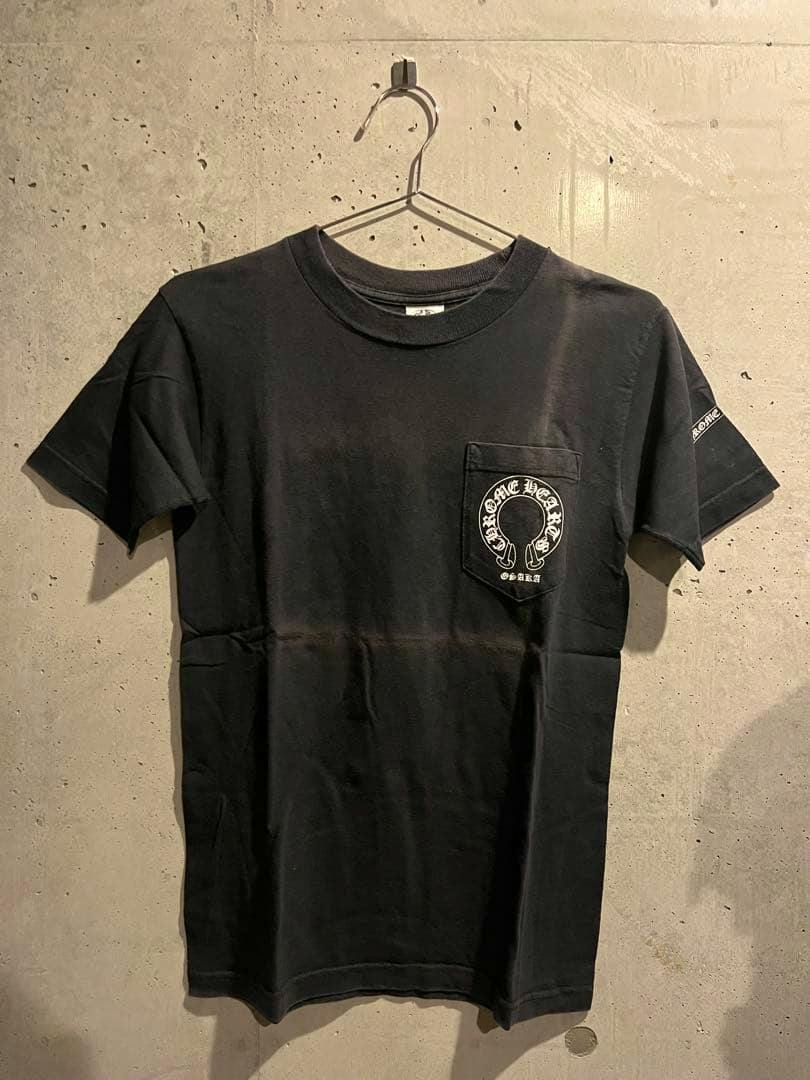 Front view of a black Chrome Hearts Osaka pocket T-shirt hanging on a hanger against a concrete wall.
