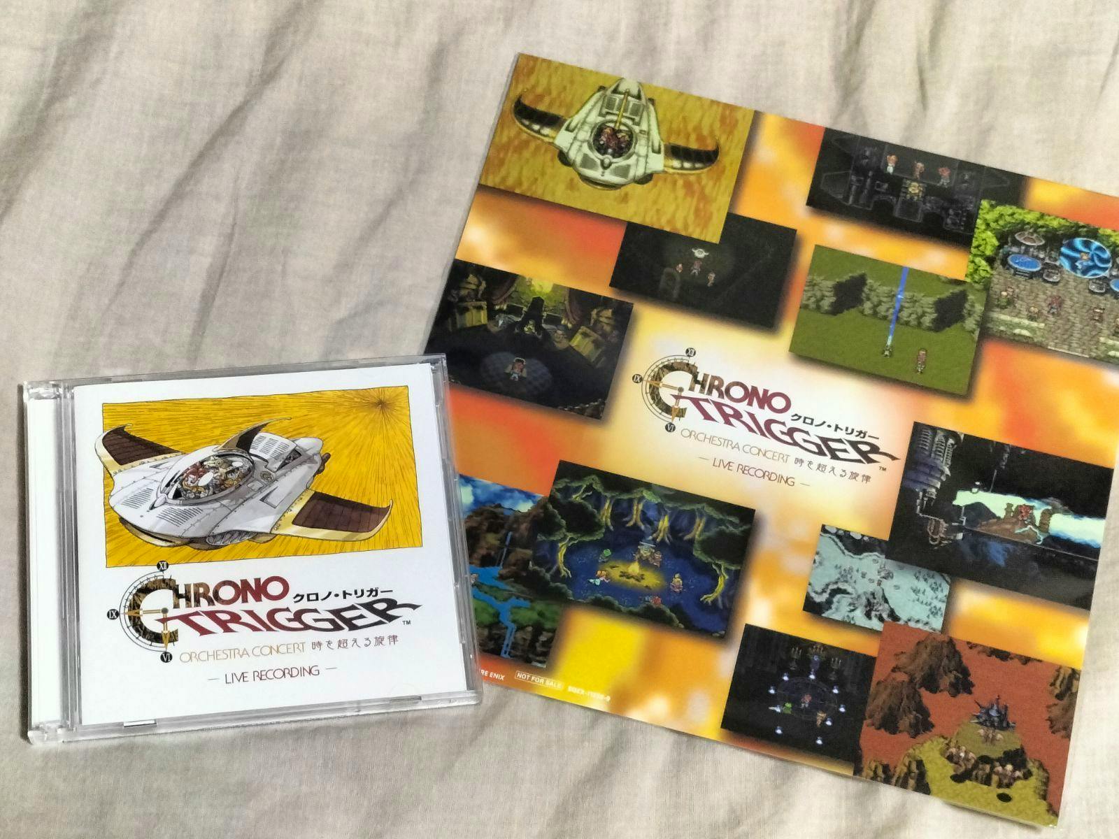 A Chrono Trigger Orchestra Concert CD jewel case and a large illustrated mega-jacket shown on a fabric background.