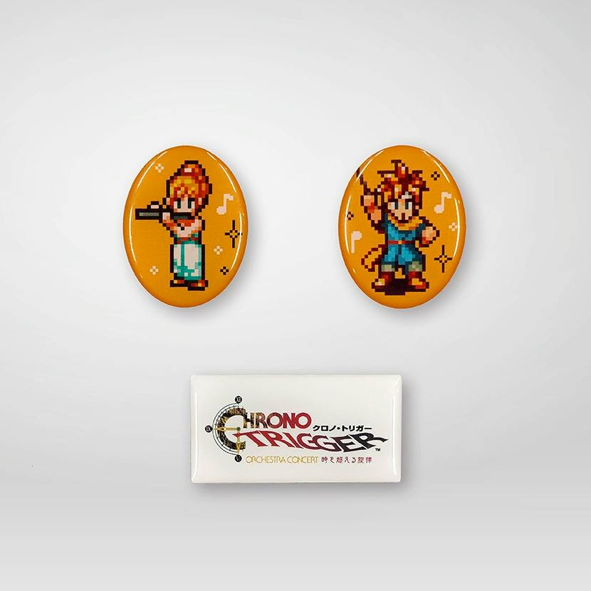 Two oval orange pins with pixel-art character designs and a white rectangular pin showing the Chrono Trigger Orchestra logo on a light background.